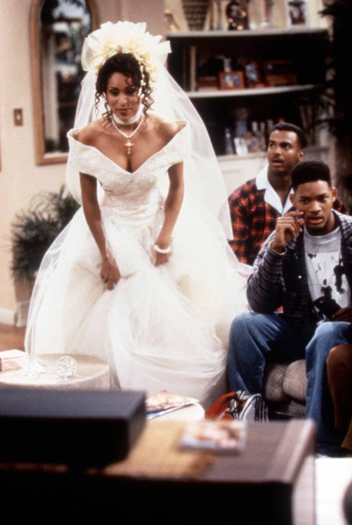 Hilary wearing a wedding dress as Will and Carlton look on during a scene