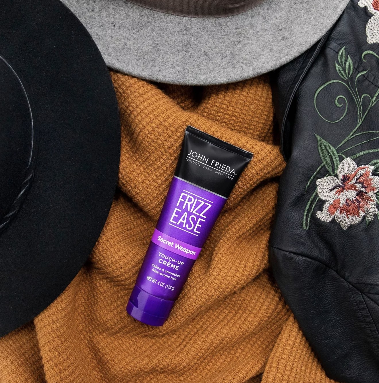 A tube of hair creme on top of an orange sweater with a black jacket and two hats