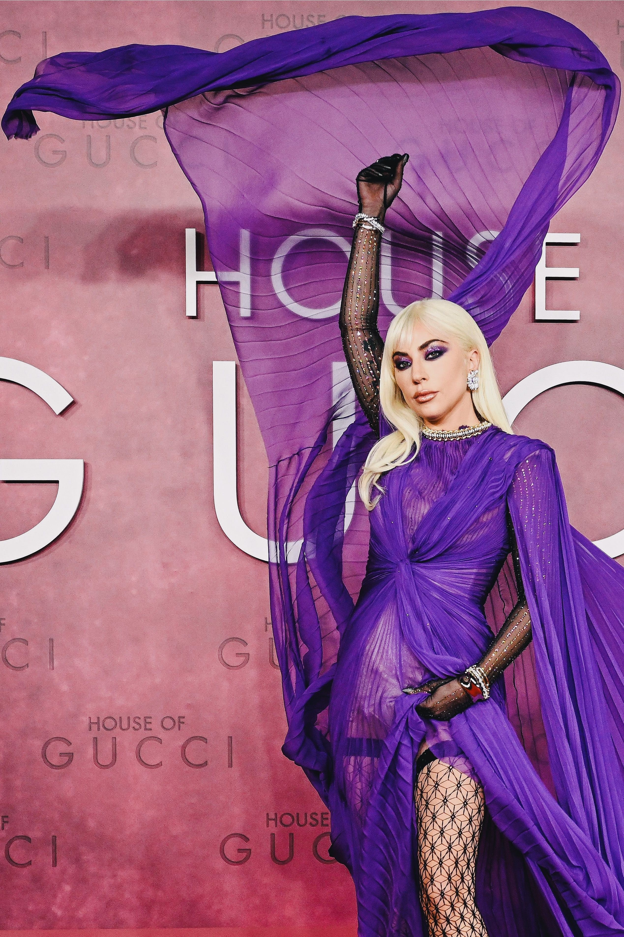 Gaga throwing on side of her gown in front of a House of Gucci logo