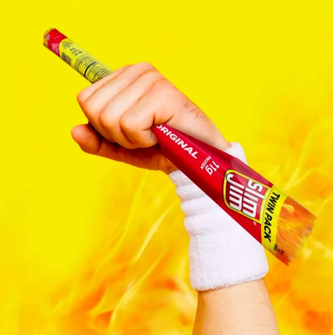 A hand triumphantly clenching a slim jim pack with flames in the background