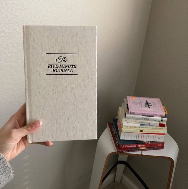 A reviewer holds up the journal in white in front of their book collection