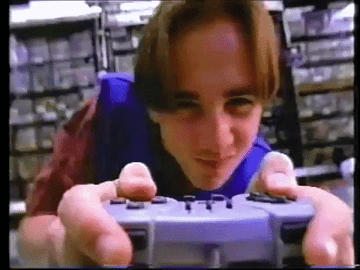 Nostalgic GIF of a kid wearing a blue Wal-Mart uniform looks at the screen and vigorously plays on a Game Boy controller