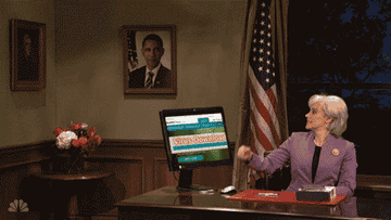 SNL gif of a man approaching a desk where a woman sits. He has a bat in his hand and smashes the computer on the desk with the bat.