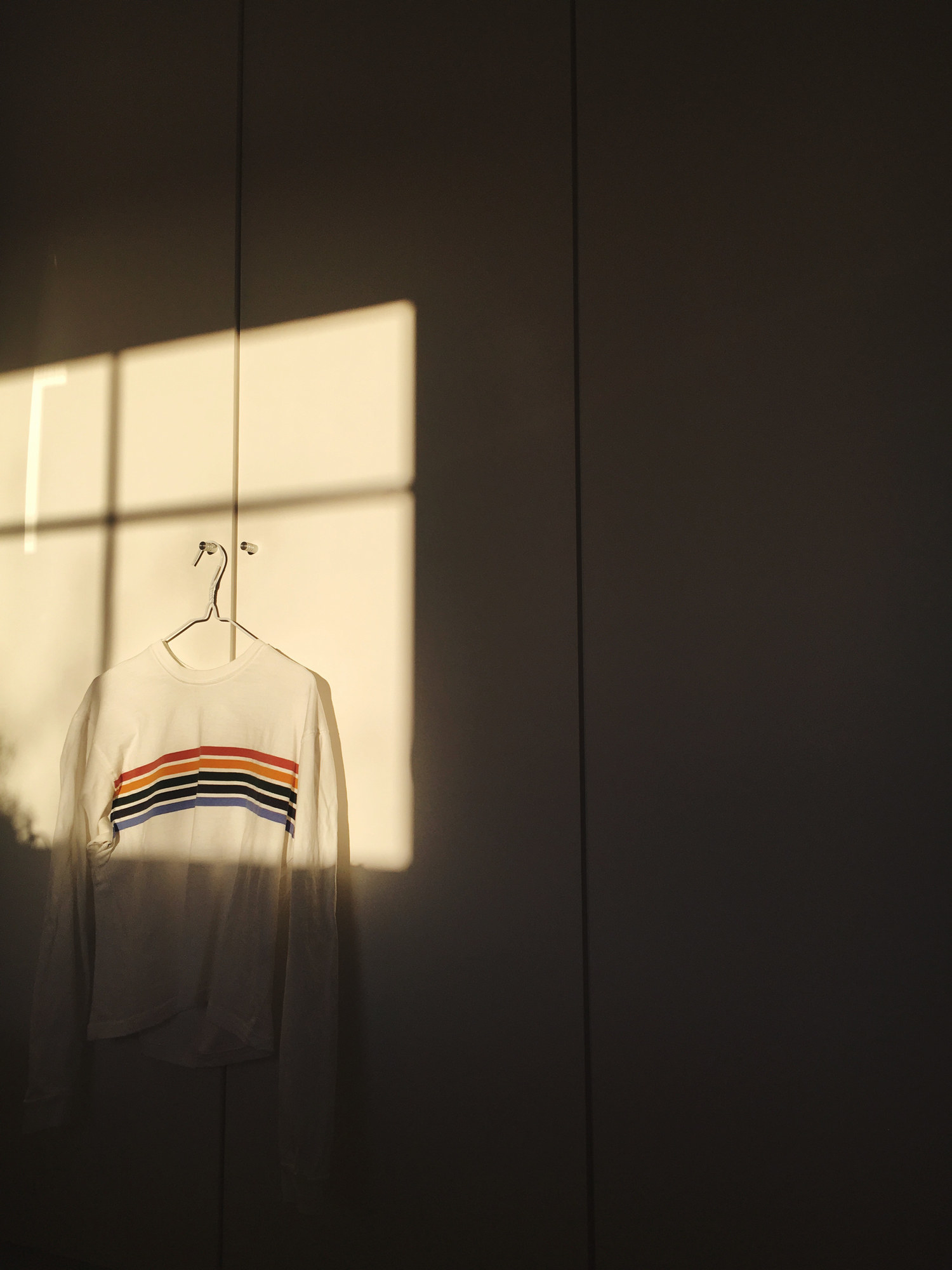 Rainbow sweater hanging on wall at home in the sunlight from window