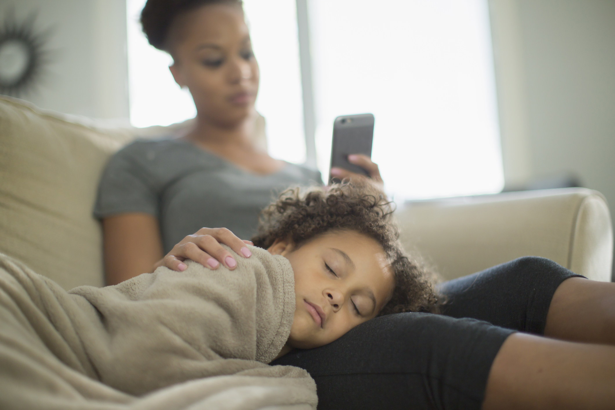 A parent checks their phone while a child naps on their lap