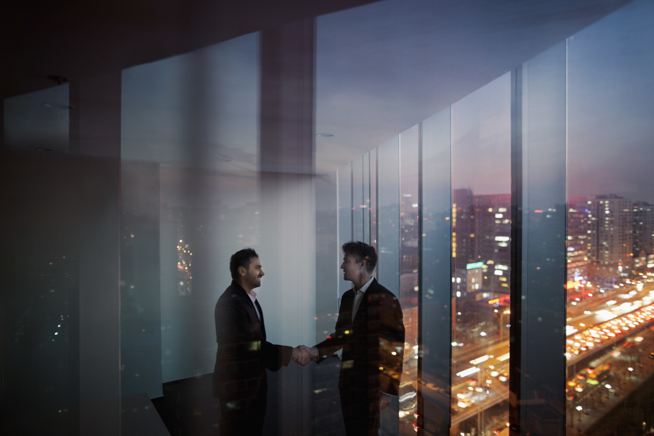 Businessmen shaking hands in conference meeting room in contemporary modern office at night