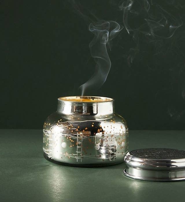 silver glass jar candle with lid next to it and a candle burning inside