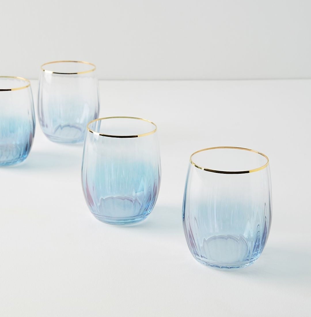 four blue/purple stemless wine glasses with a gold rim