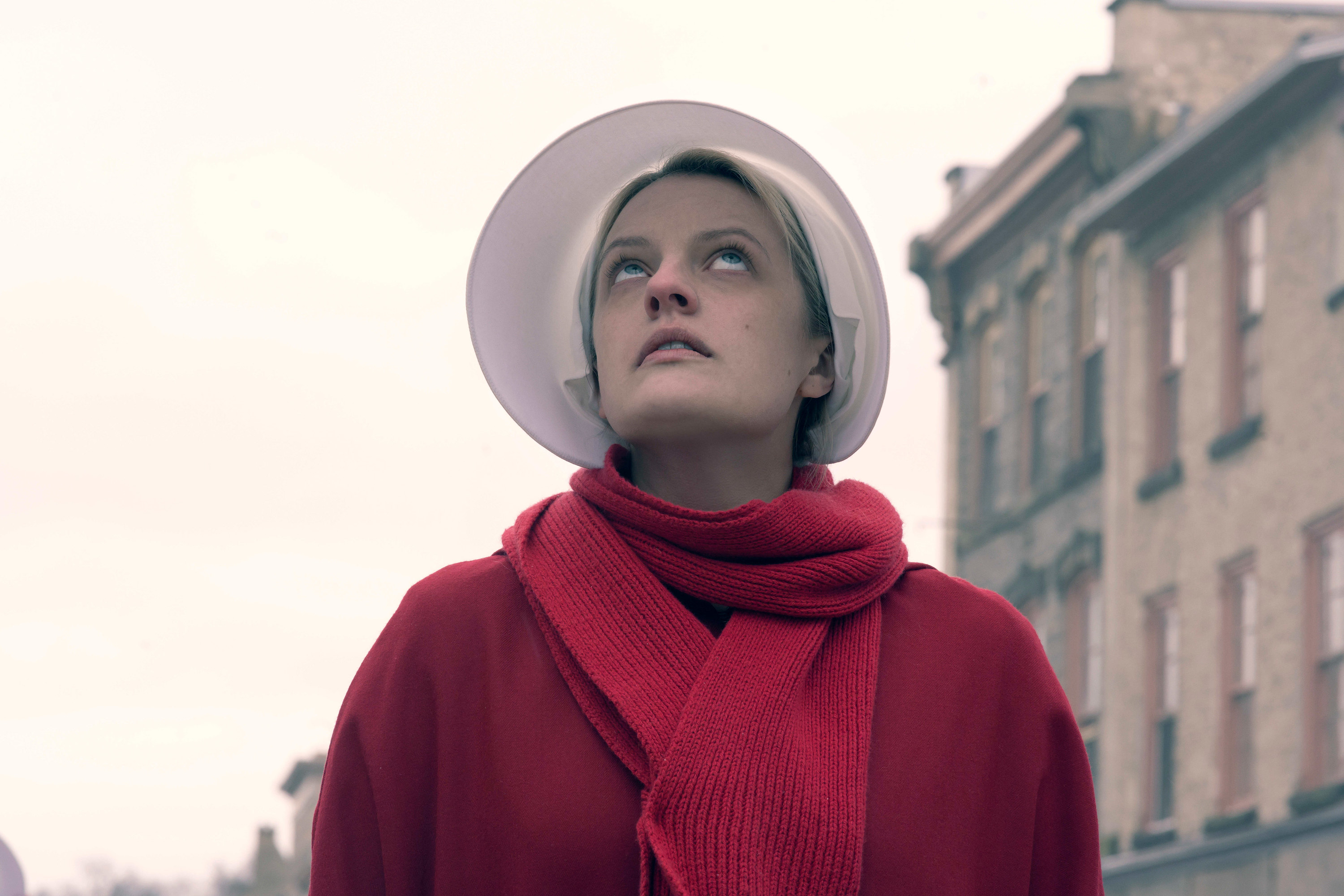 Elizabeth Moss outside in her red dress and bonnet looking upward
