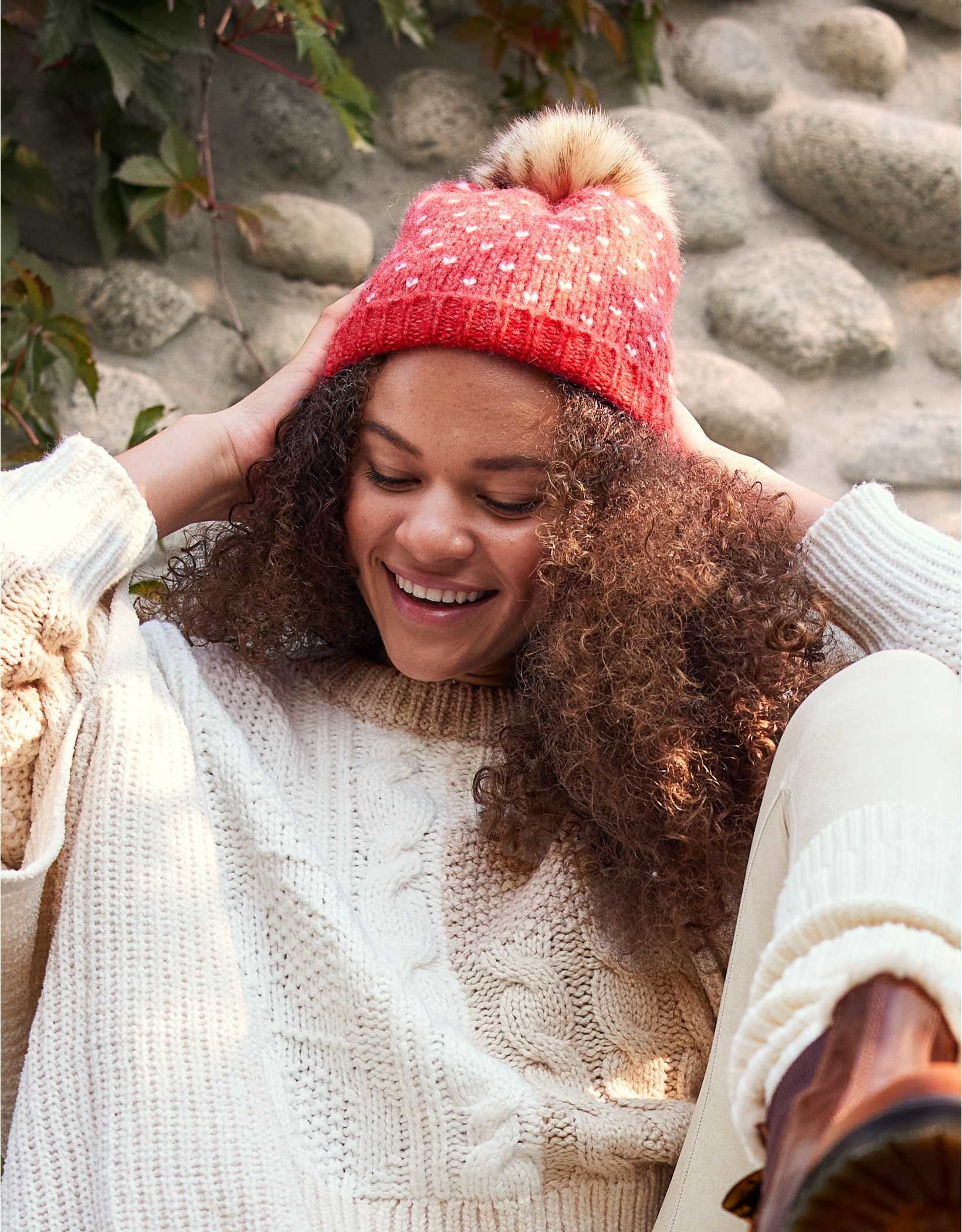 model in dark pink knit hat with white dots and a brown faux fur pompom