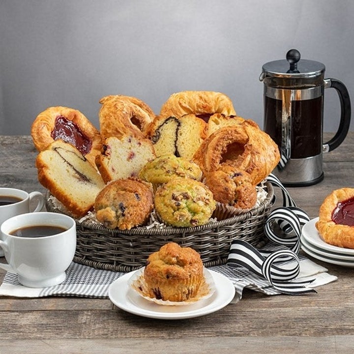 Assortment of pastries and muffins in a basket with a coffee maker and cups on a wooden table, suggesting a breakfast setup