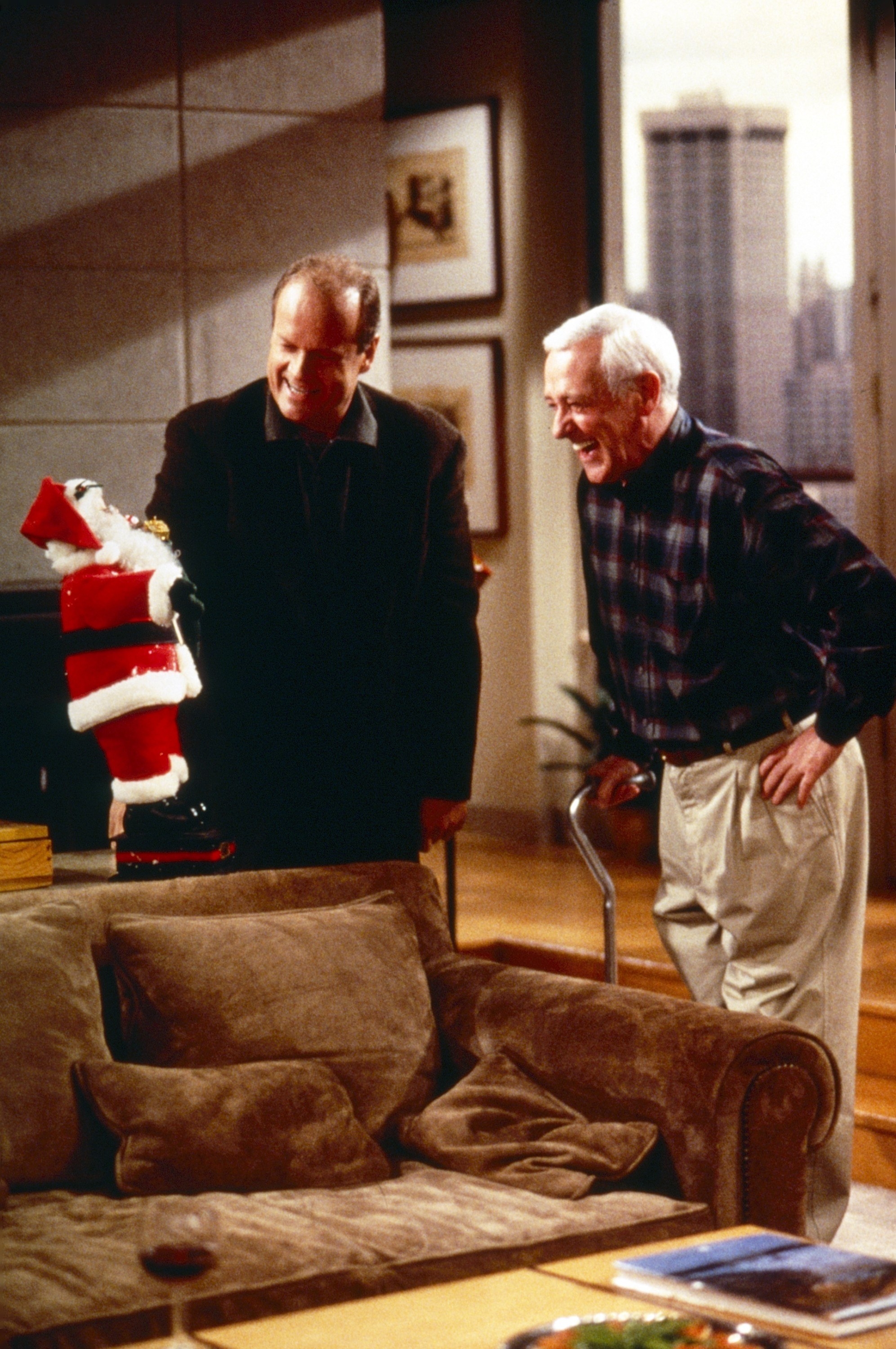 Kelsey Grammer, John Mahoney laughing while looking at a toy santa claus on a table
