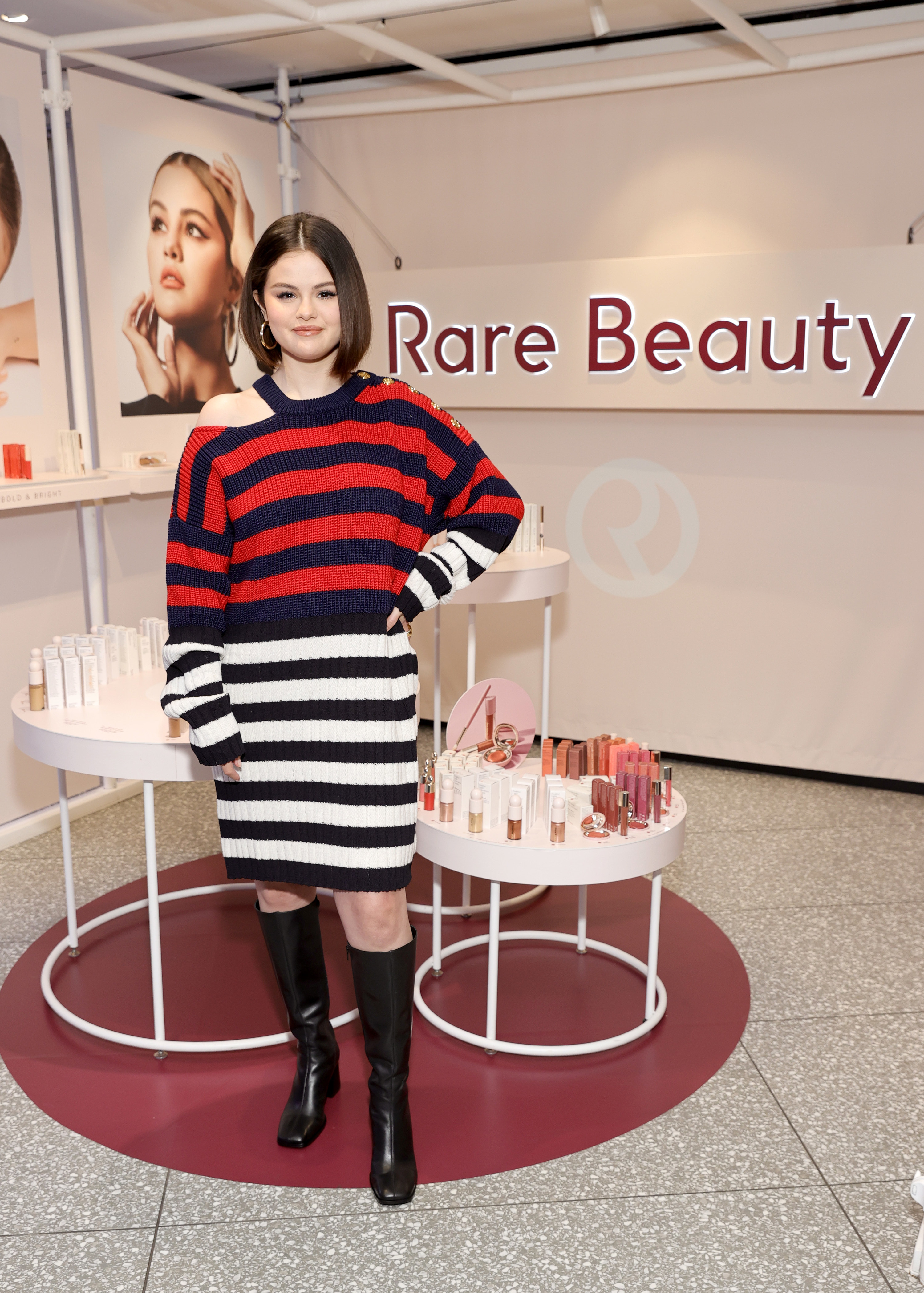 Selena stands in front of a display for her cosmetics brand Rare Beauty