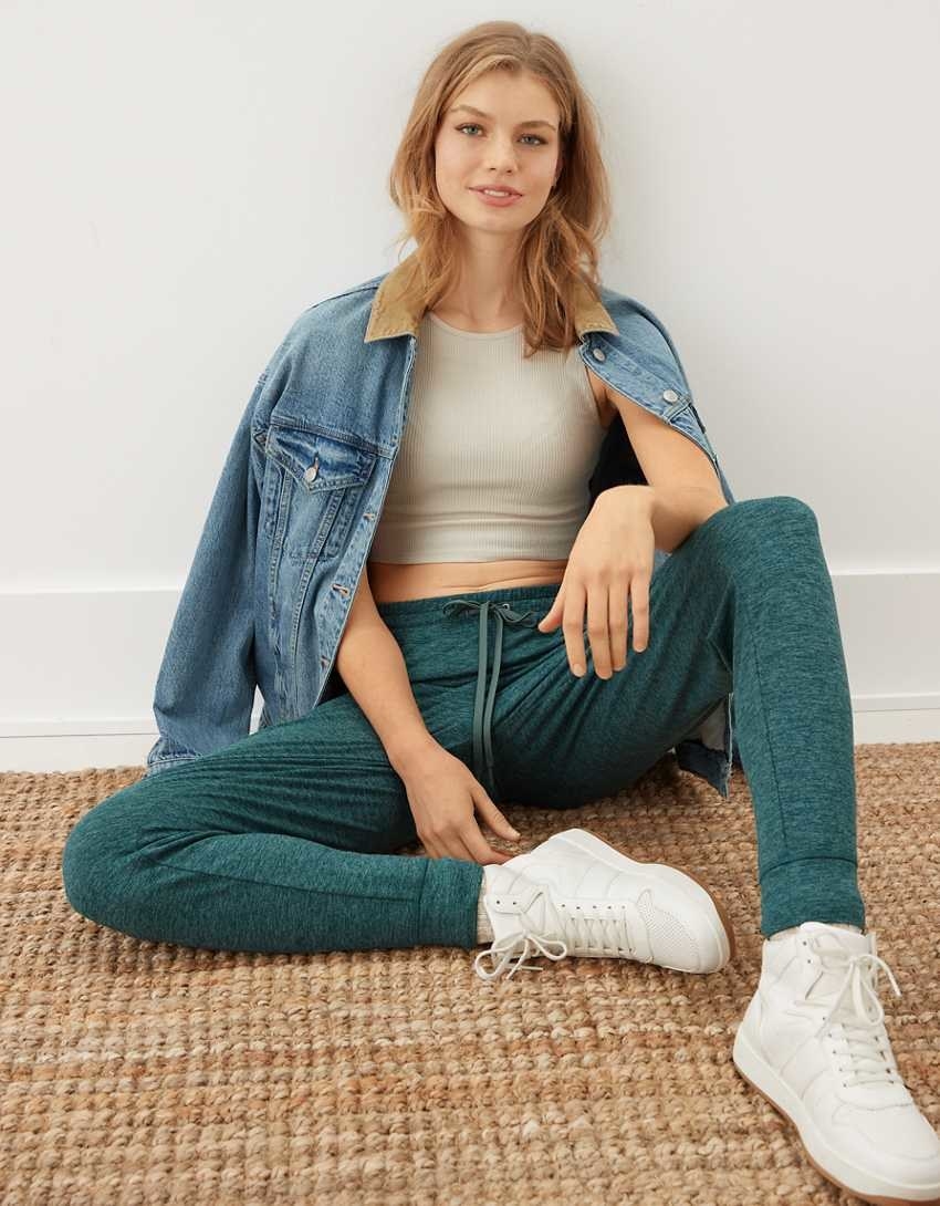 Model lounging in the teal joggers with crop top and jean jacket