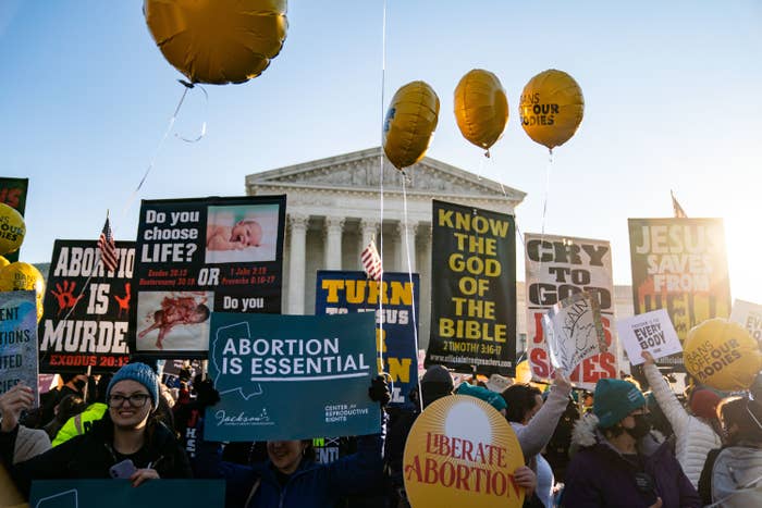 Opposing demonstrators carry signs that read "abortion is essential," "liberate abortion," "abortion is murder," and "know the god of the people"