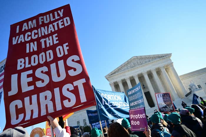 People carry signs that read "I am vaccinated in the blood of Jesus Christ," "Protect Roe," and "Abortion is essential"