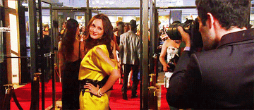 Blair Waldorf, wearing a brightly colored silk dress, poses for a flashing camera