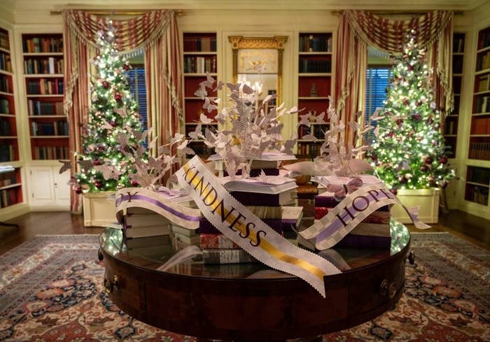 A round table filled with stacks of books with banners that say &quot;Kindness&quot; and &quot;Hope&quot; in a room in the White House with Christmas trees in the background