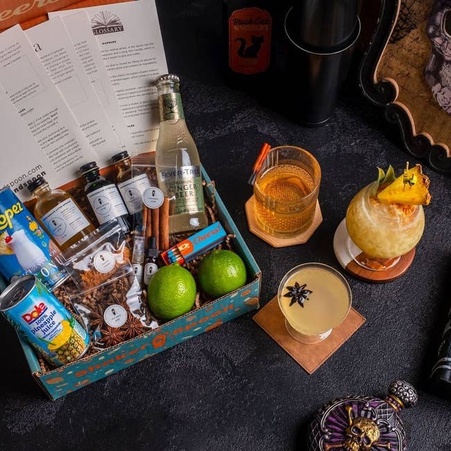 a top-down view of an open box filled with drink ingredients next to three cocktails