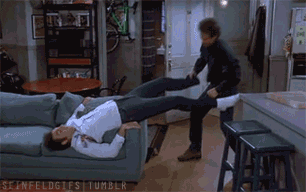 Seinfeld trying to pull a pair of tight pants off of Kramer who&#x27;s lying down on the couch