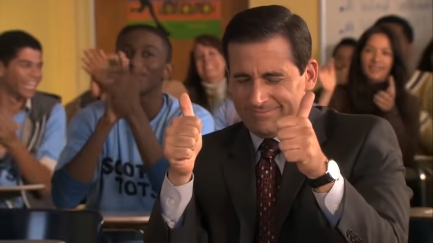 Michael smiling awkwardly with his thumbs up in a classroom with other clapping students in &quot;The Office&quot;