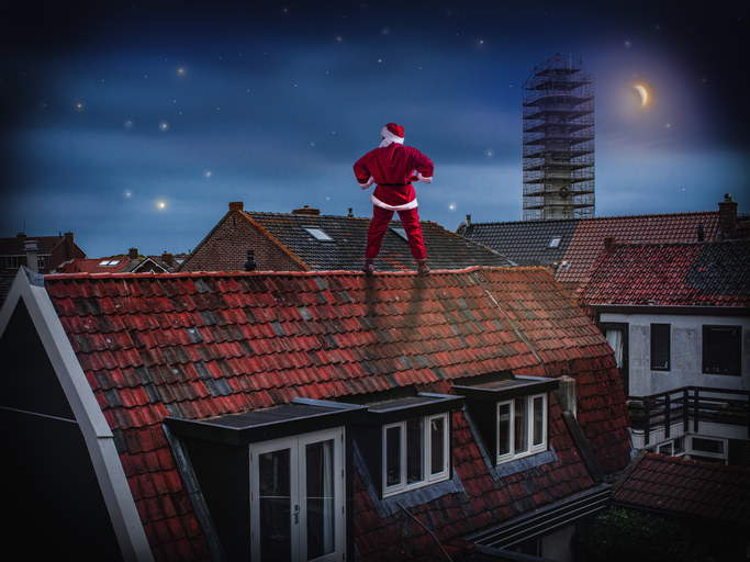 Night scene with the moon. Successful Santa Claus stands on the roof of an old house with his hands on his hips