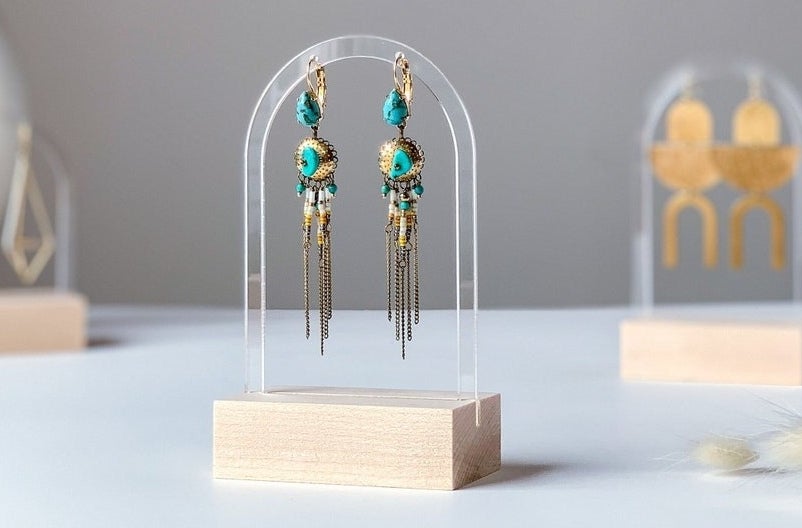 A pair of turquoise and gold earrings hanging on a clear acrylic stand with a wooden base