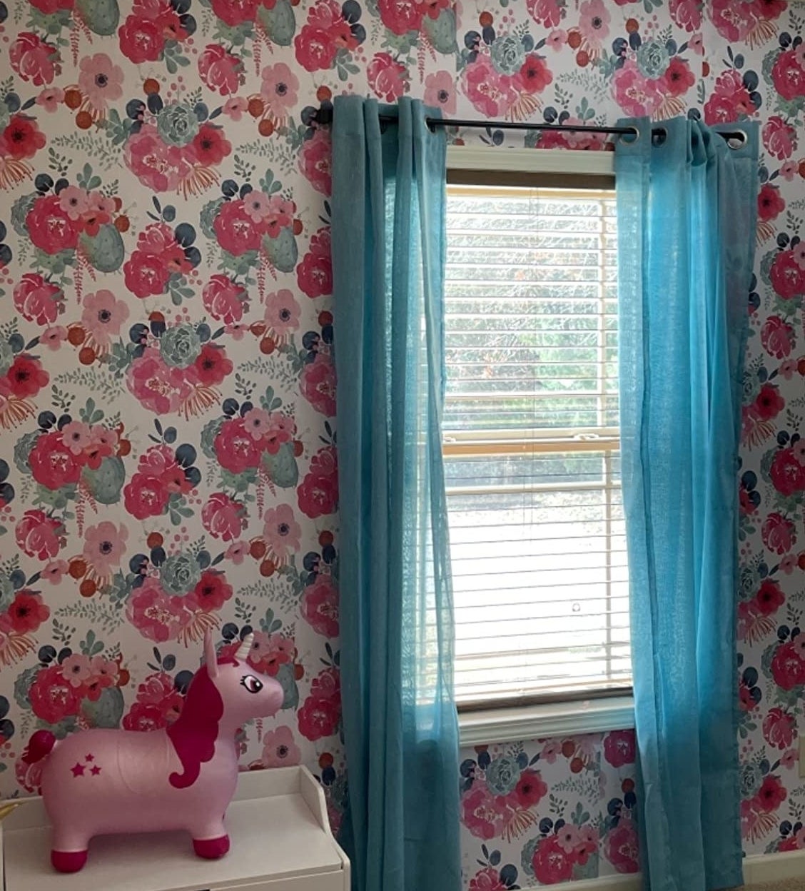 Reviewer image of pink floral wallpaper next to window with blue curtains