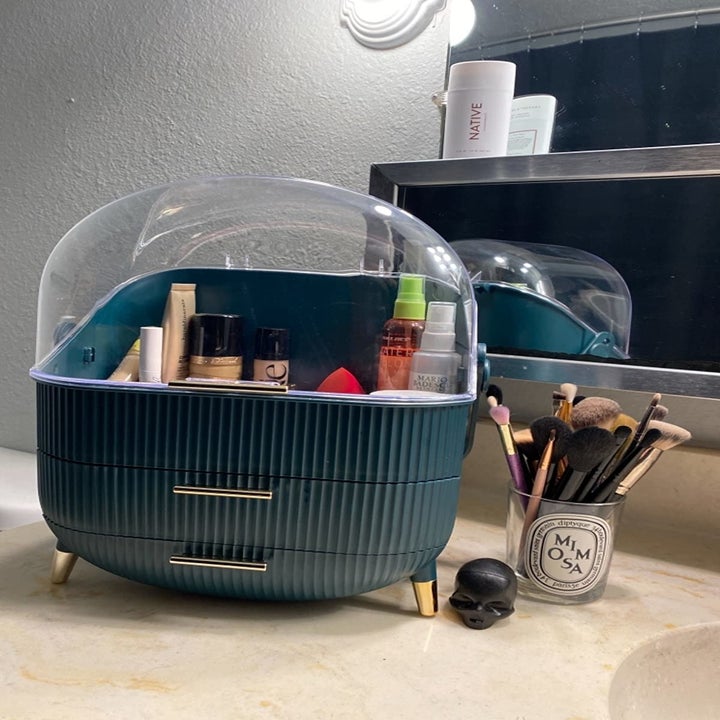 a reviewer shows the green organizer with their beauty products inside