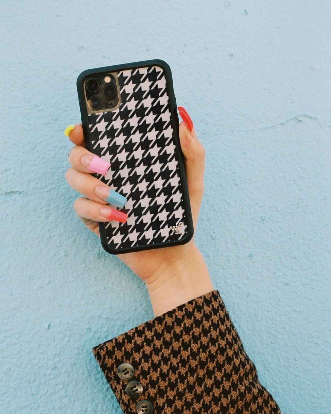 someone holding up the houndstooth patterned phone case against a colourful wall
