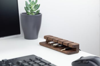 the dark wood organizer holding four different cords on a white desk