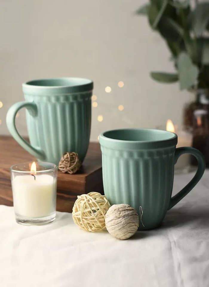 Two green mugs on a table next to a candle