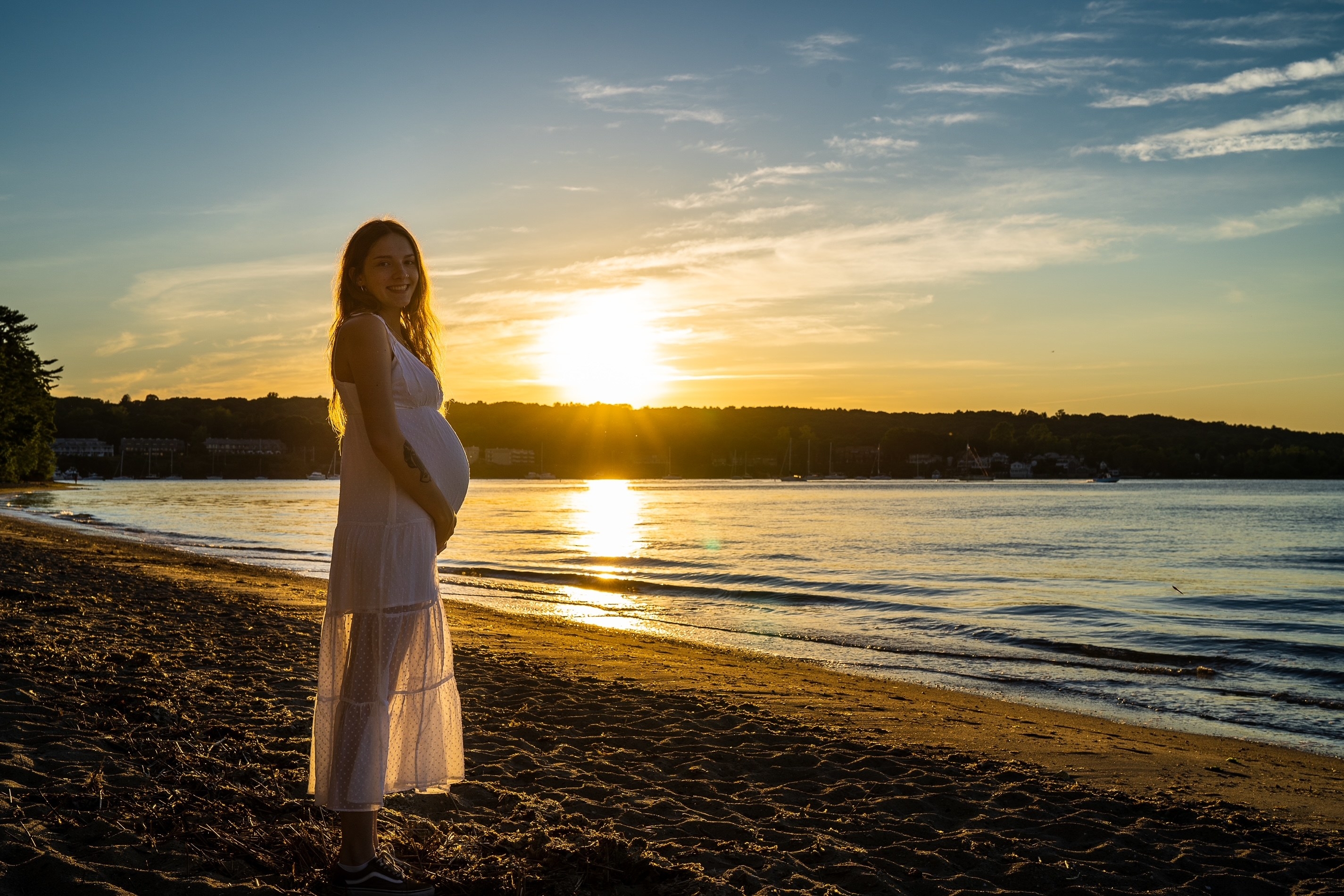 Marissa standing at the beach at sunset cradling her baby bump