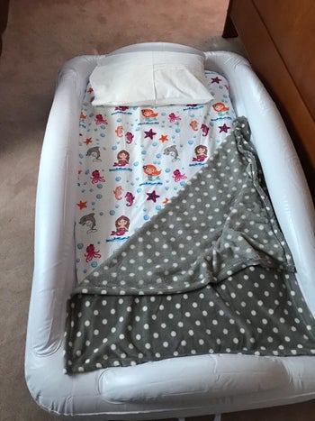 reviewer's photo of the inflatable bed with a mermaid bedsheet and polka dot blanket