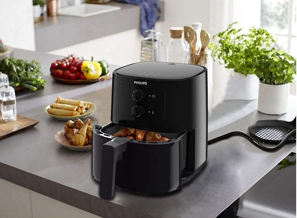 An air fryer on a table with food beside it on plates