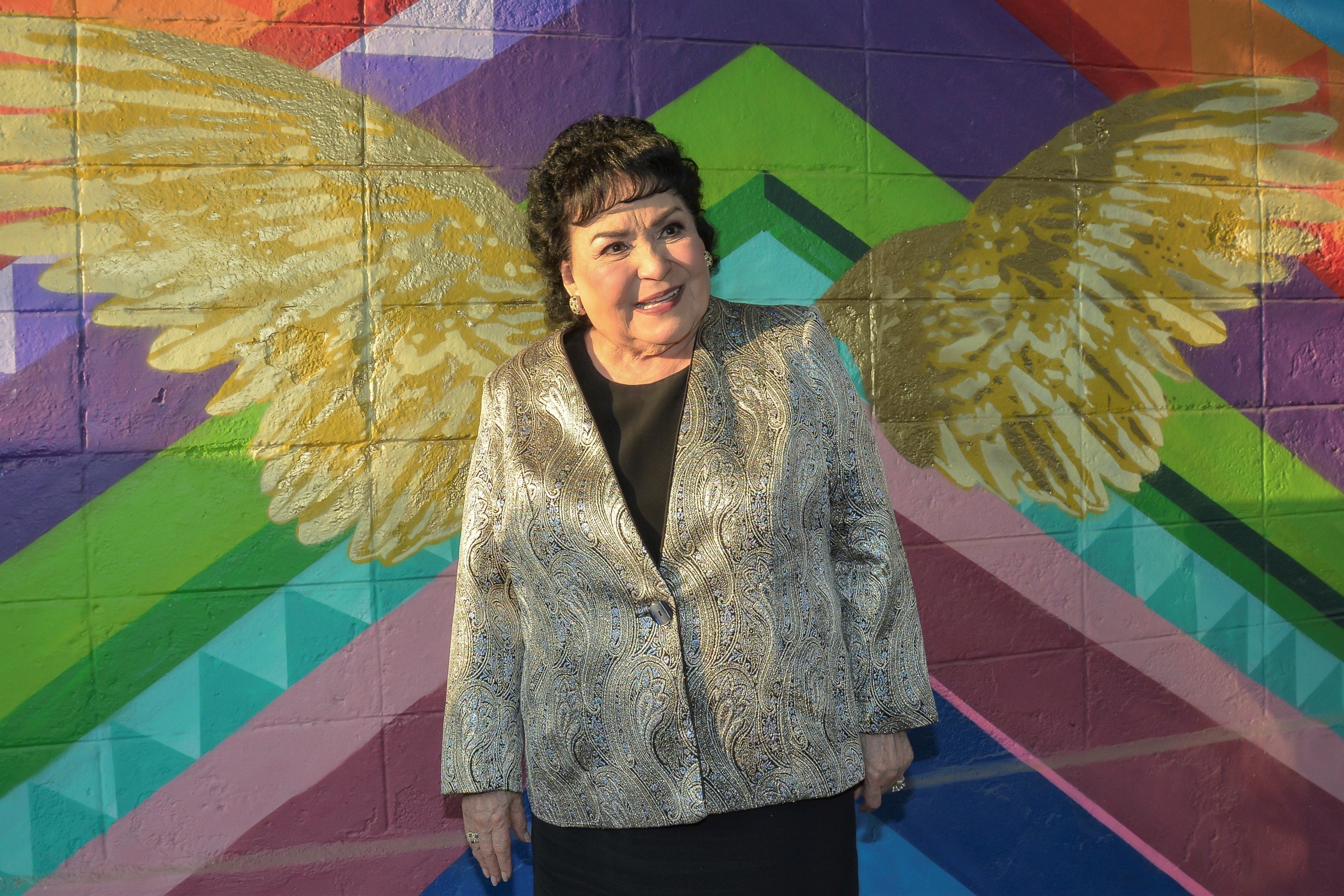 Carmen smiling while standing in front of an angel wings mural