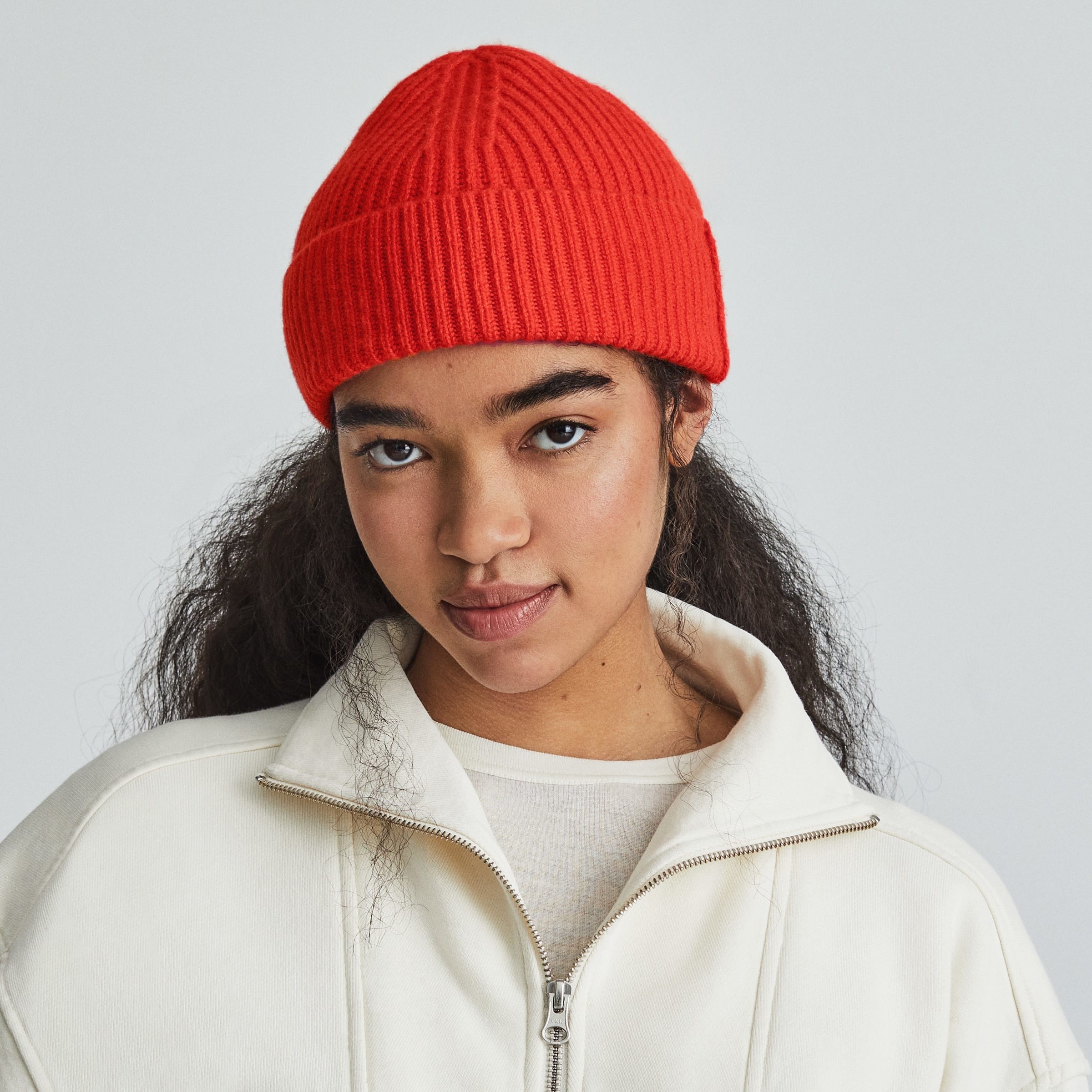model in bright red beanie and cozy white half-zip pullover