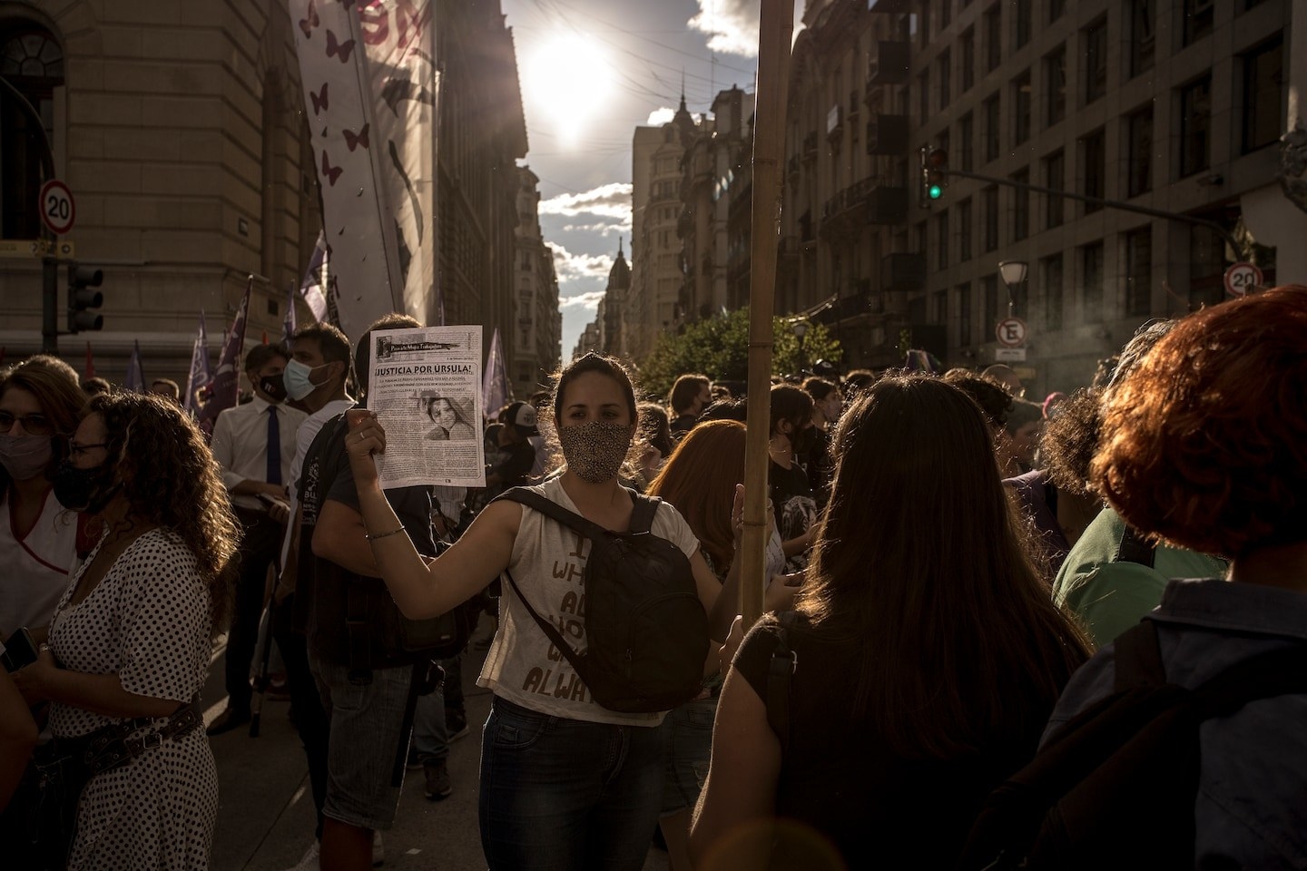 A woman in a mask holds up a sign for a missing woman in a crowd of people walking past her