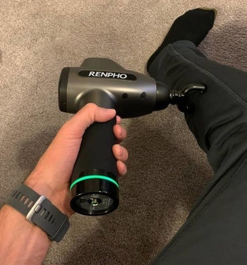 hand holds silver and black Renpho massage gun to massage sore calf