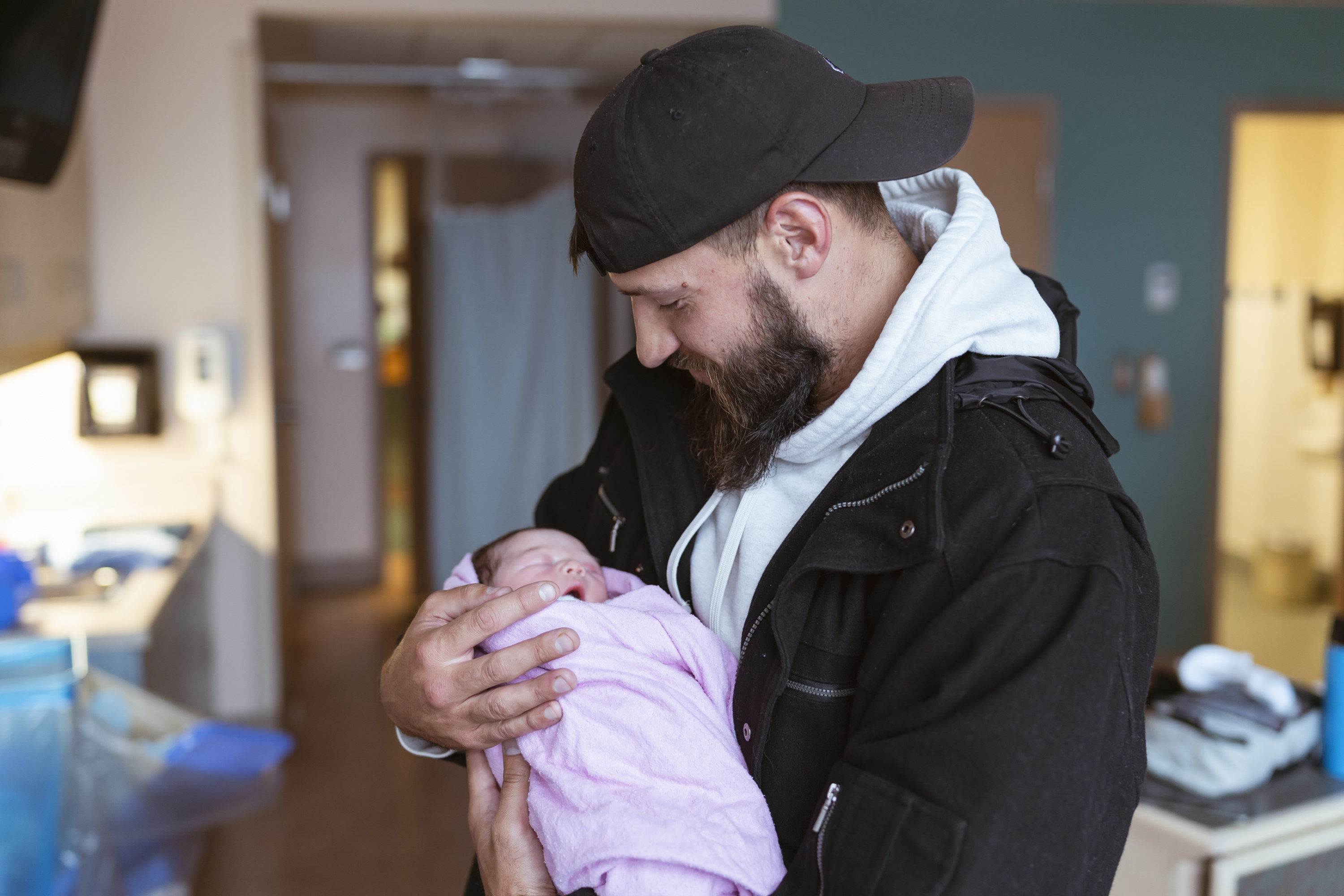 A man wearing a black hat and jacket holding a newborn baby