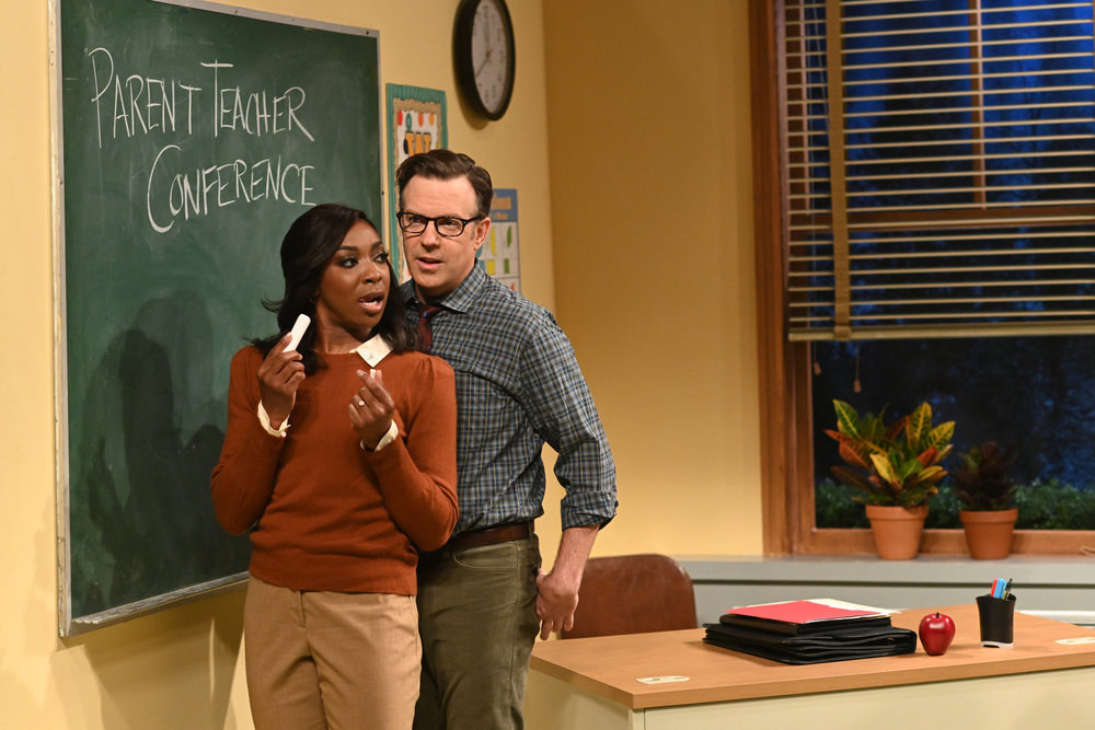 Ego Nwodim as a mother stands beside a chalkboard as she holds piece of chalk and leans on Jason Sudeikis as a teacher in &quot;Saturday Night Live&quot;