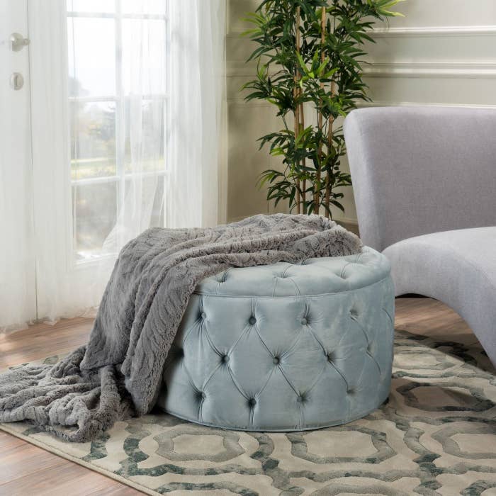 The ottoman in light gray with a throw blanket on it