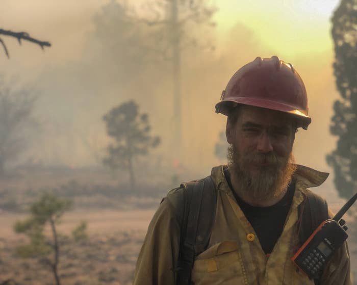 a man in a fire helmet and firefighter gear with smoke behind him 