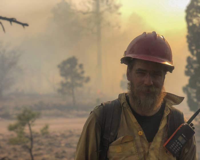 a man in a fire helmet and firefighter gear with smoke behind him