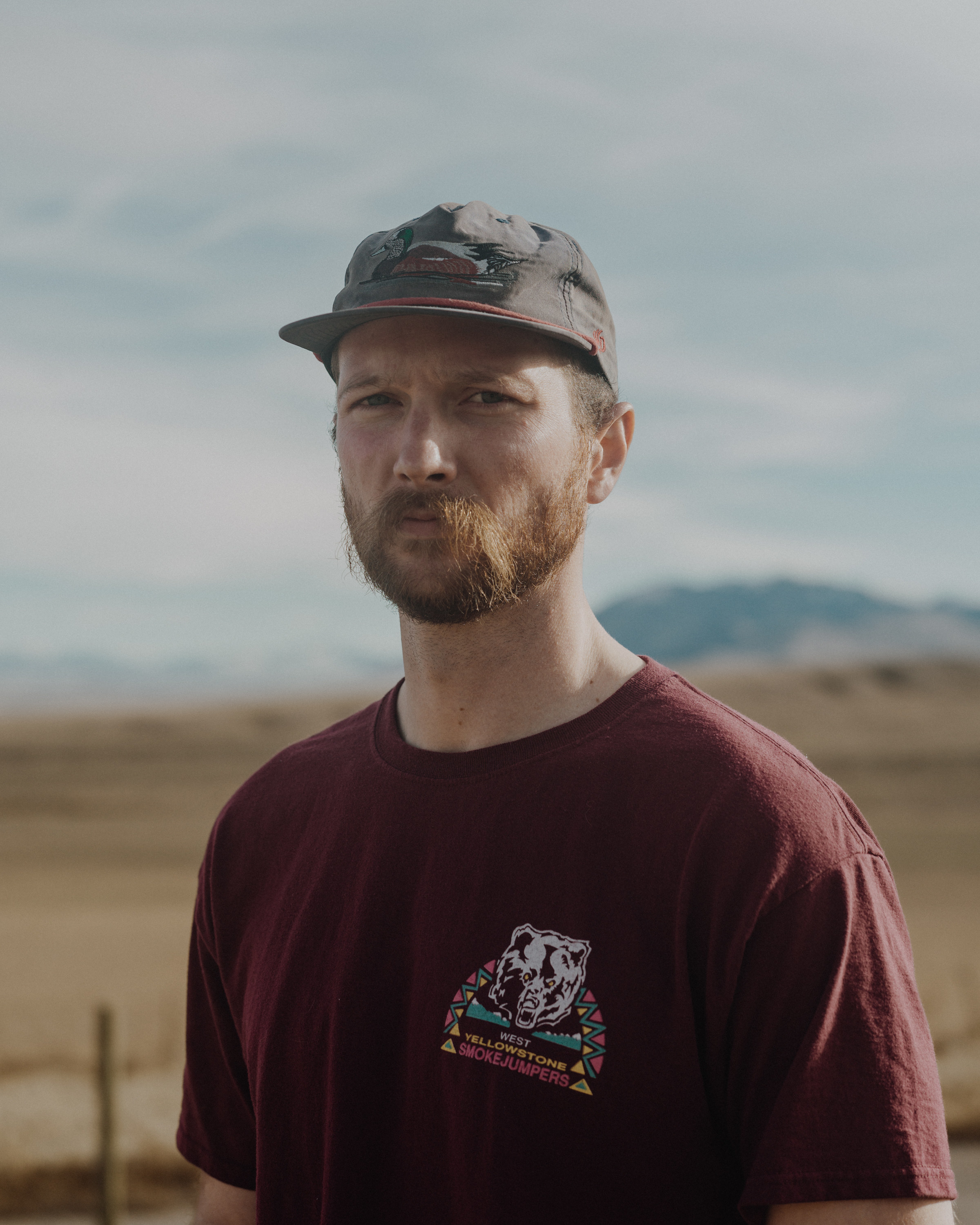 a man in a smokejumper t-shirt and baseball hat in a landscape