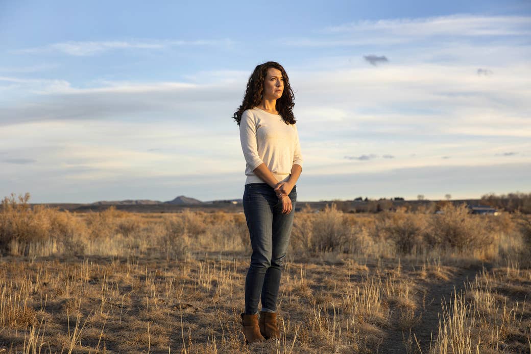 a woman stand alone in a field with mountains behind her and a cloudy sky