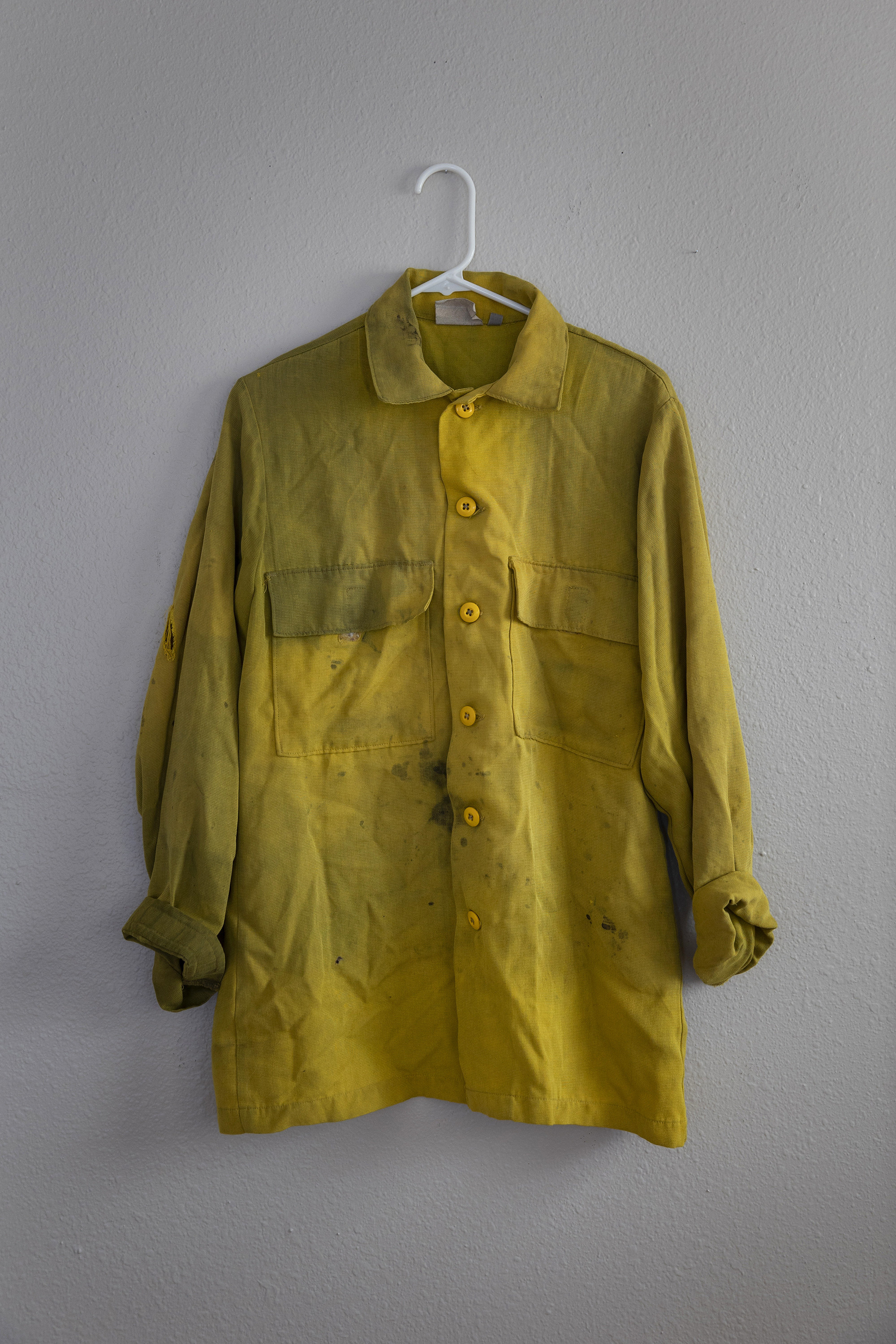 A yellow shirt photographed on a white wall