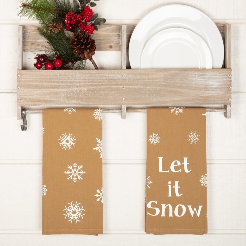 Brown tea towels hanging from towel rack with white snowflakes and &quot;let in snow&quot; in white lettering