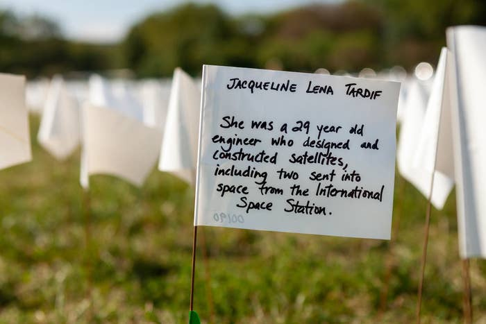 A small white flag planted in the grass reads "Jacqueline Lena Tardif: She was a 29 year old engineer who designed and constructed satellites, including two sent into space from the International Space Station"