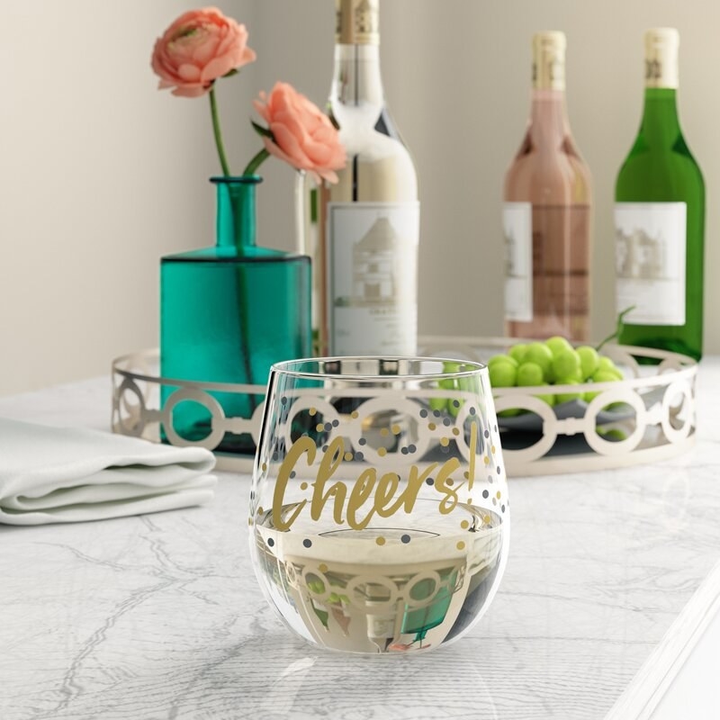 White wine in stemless wine glass that says cheers with gold and black decoration